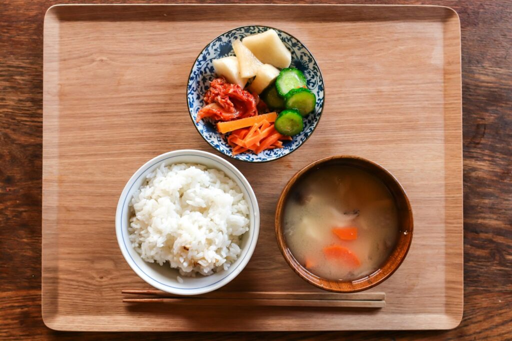 木のトレーに並んだご飯、みそ汁、漬物の和食